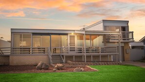 A modern two-story house with large windows, a balcony, and a well-maintained lawn. - Sand Castles - 34 Gold Coast Drive (CARRICKALINGA)