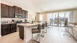 Una cocina moderna con armarios oscuros, una isla central y un comedor con mesa y sillas de vidrio.