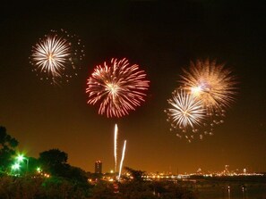 A nighttime view of fireworks over a cityscape with a body of water in the foreground.