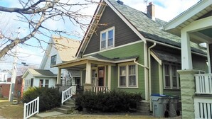 A two-story house with a green exterior, a front porch, and a visible staircase leading to the entrance. - Comfortable 3BR Craftsman Bungalow in Milwaukee Bay View Neighborhood Sm Dog OK (Milwaukee)