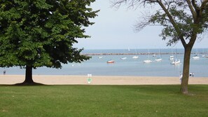 A beach with a tree in the foreground and boats in the water.