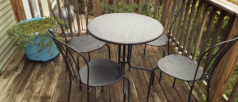 Una terraza de madera con una mesa redonda de metal y cuatro sillas.