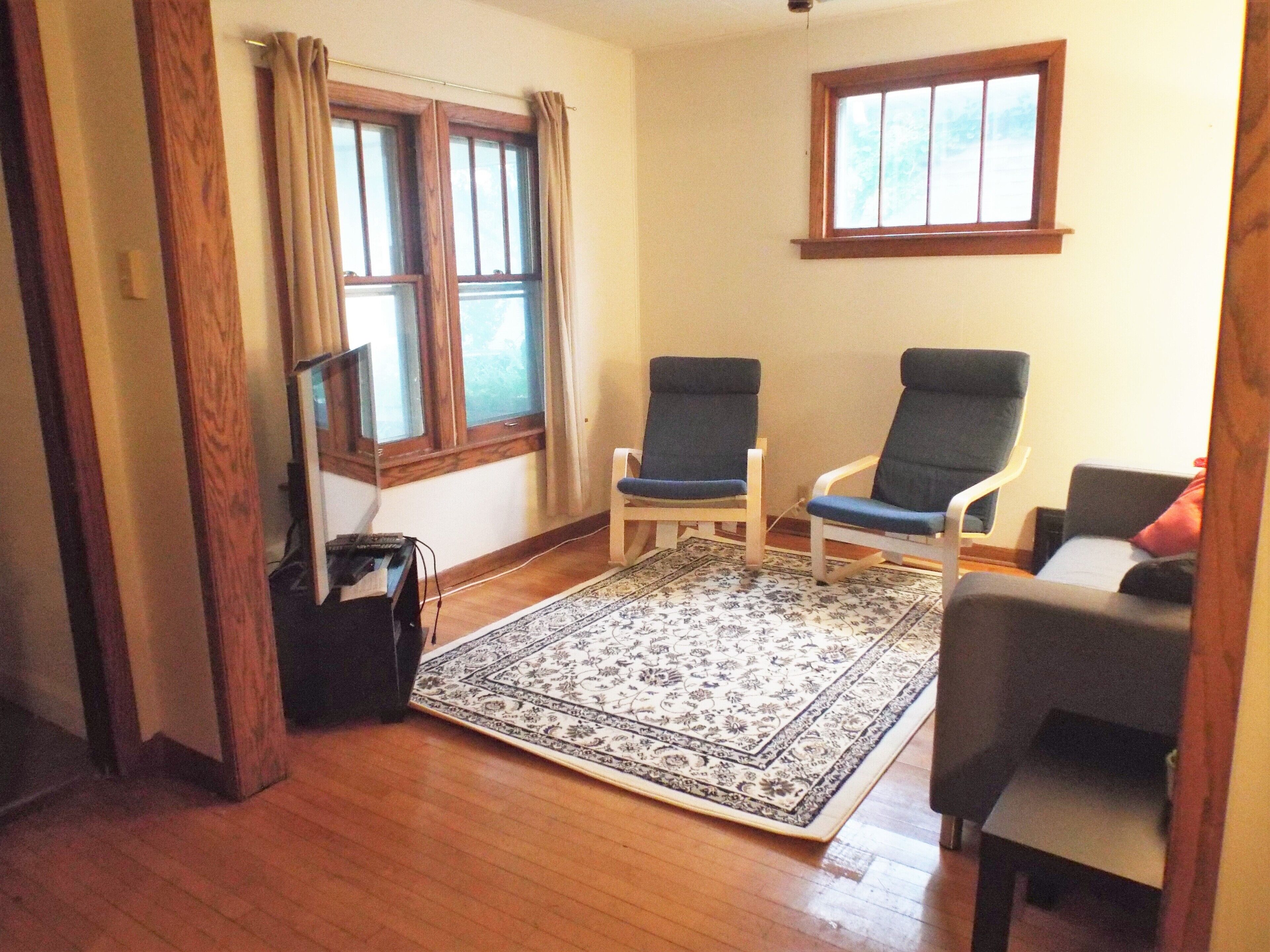 A room with two chairs, a small rug, wooden flooring, and a window.