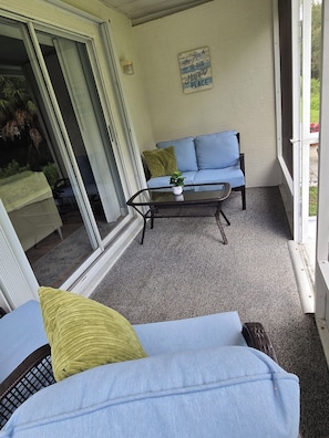 A balcony with a glass door, a blue sofa, a small table with a plant, and a sign on the wall.