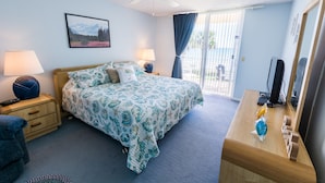A bedroom with a bed, nightstands, a dresser, a ceiling fan, a window with curtains, and a picture on the wall. - Oceanfront 2BR Condo 2nd Floor Balcony with Beautiful Beach Views, Unit 203 (Indian Harbour Beach)