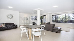 Una sala de estar moderna con una mesa redonda, sillas blancas, un sofá gris y una estantería.