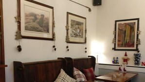 A cozy dining area with a wooden table and benches, framed pictures on the wall, and a small Christmas tree decoration. - The Victoria (Skipton)