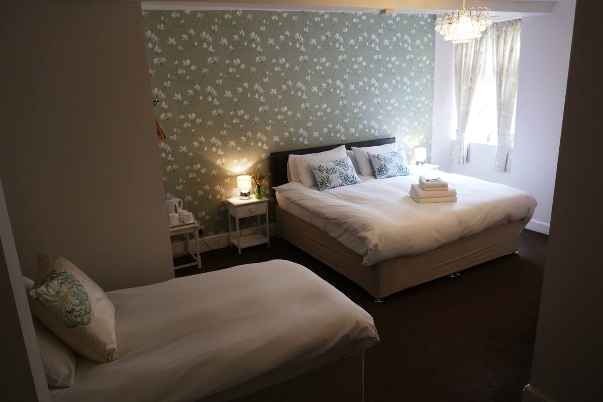 A bedroom with two beds, a nightstand, a lamp, and a window with curtains.