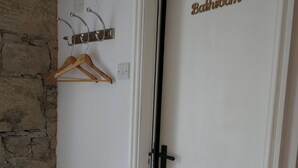 A bathroom with a white door labeled "Bathroom," a wooden coat rack, and a stone wall. - The Victoria (Skipton)