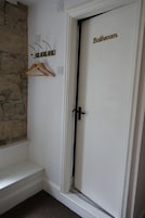 Un baño con una puerta blanca que dice 'Bathroom', un perchero de madera y una pared de piedra.