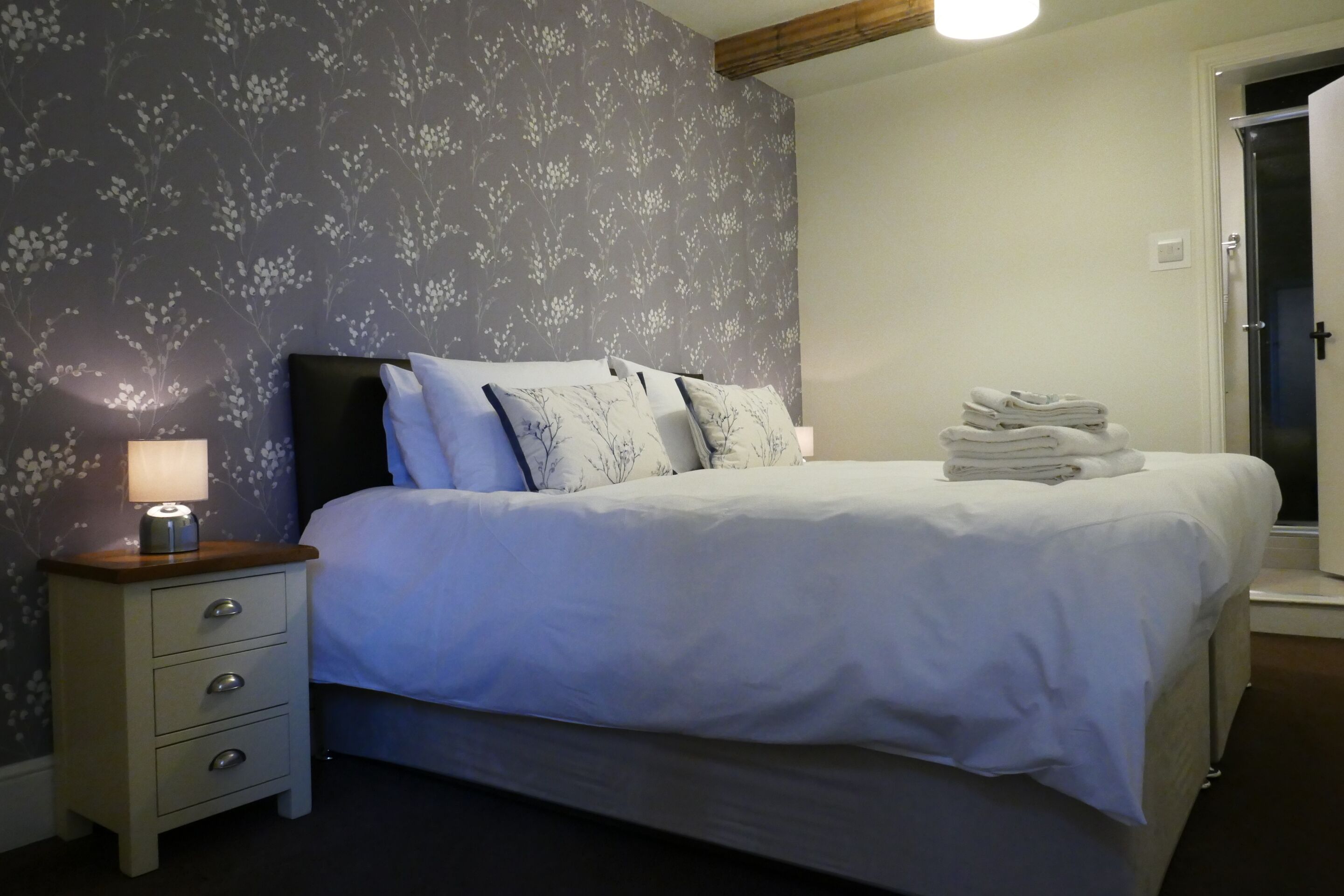 Een net opgemaakt bed met witte lakens en een klein nachtkastje met een lamp.