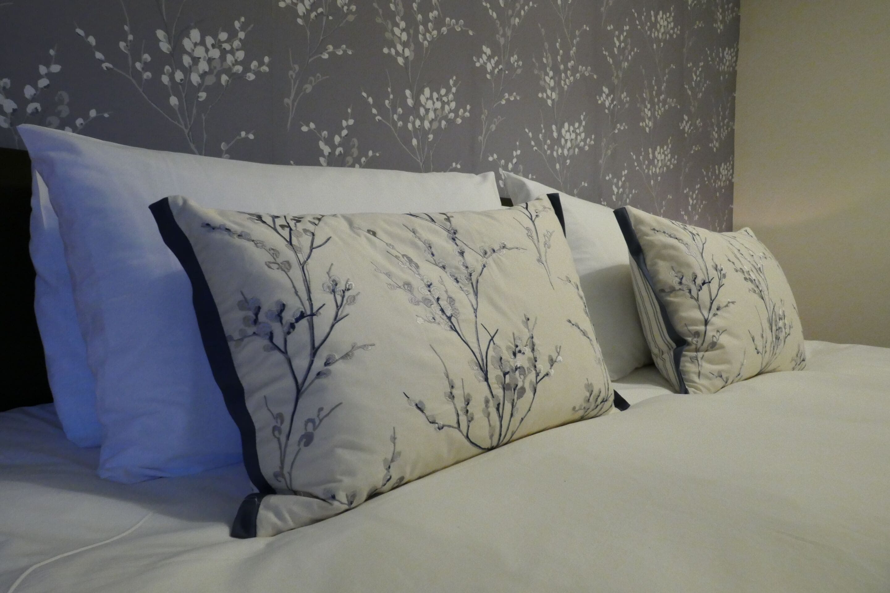 Ein Bett mit weißer Bettwäsche und drei Kissen mit Blumenmuster.