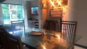 Ein moderner Essbereich mit einem Glastisch, Holzstühlen und einem Fernseher im Hintergrund.