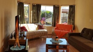A spacious living room with a wooden ceiling, large windows with curtains, a sofa, a coffee table, and a television. - Farm in Socorro wi-fi, solar heated pool, hot tub  (Socorro)