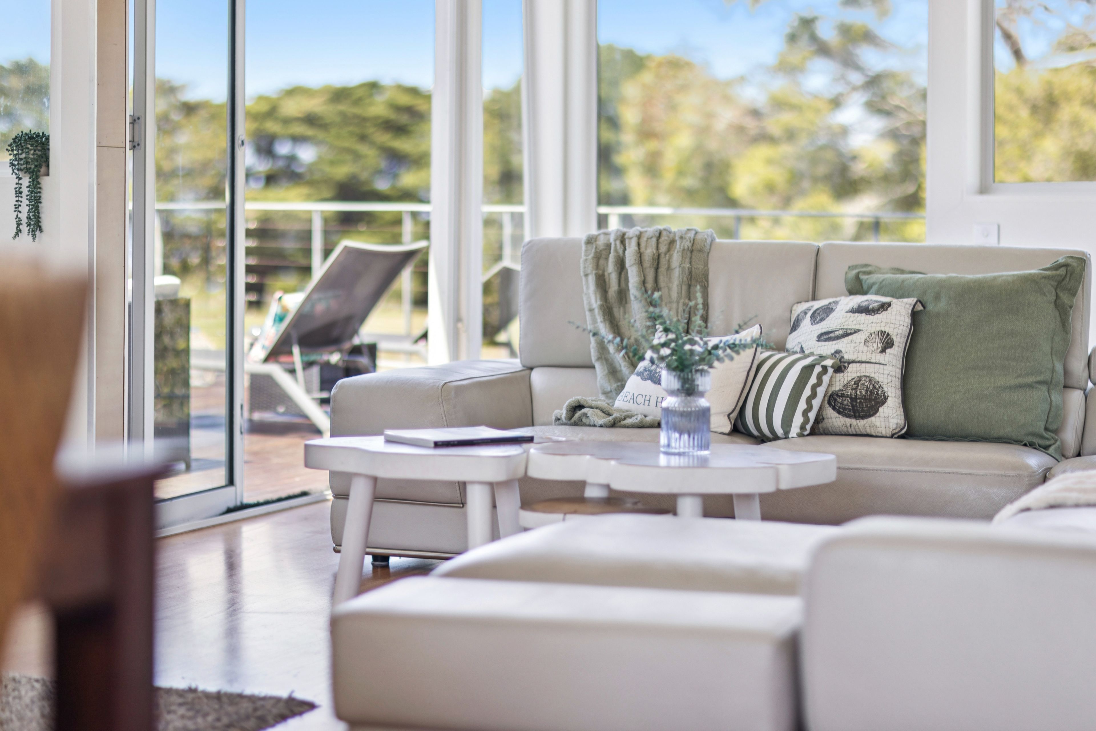 A modern living room with a sofa, a coffee table, and a chair. There is a large window providing a view of the outdoors.