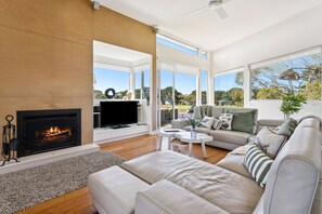 Una sala de estar moderna con chimenea, televisor de pantalla plana y un amplio ventanal con vistas al exterior.