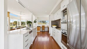 A modern kitchen with white cabinetry, a stainless steel refrigerator, and a view of the outdoors. - Fairway View (FLINDERS)