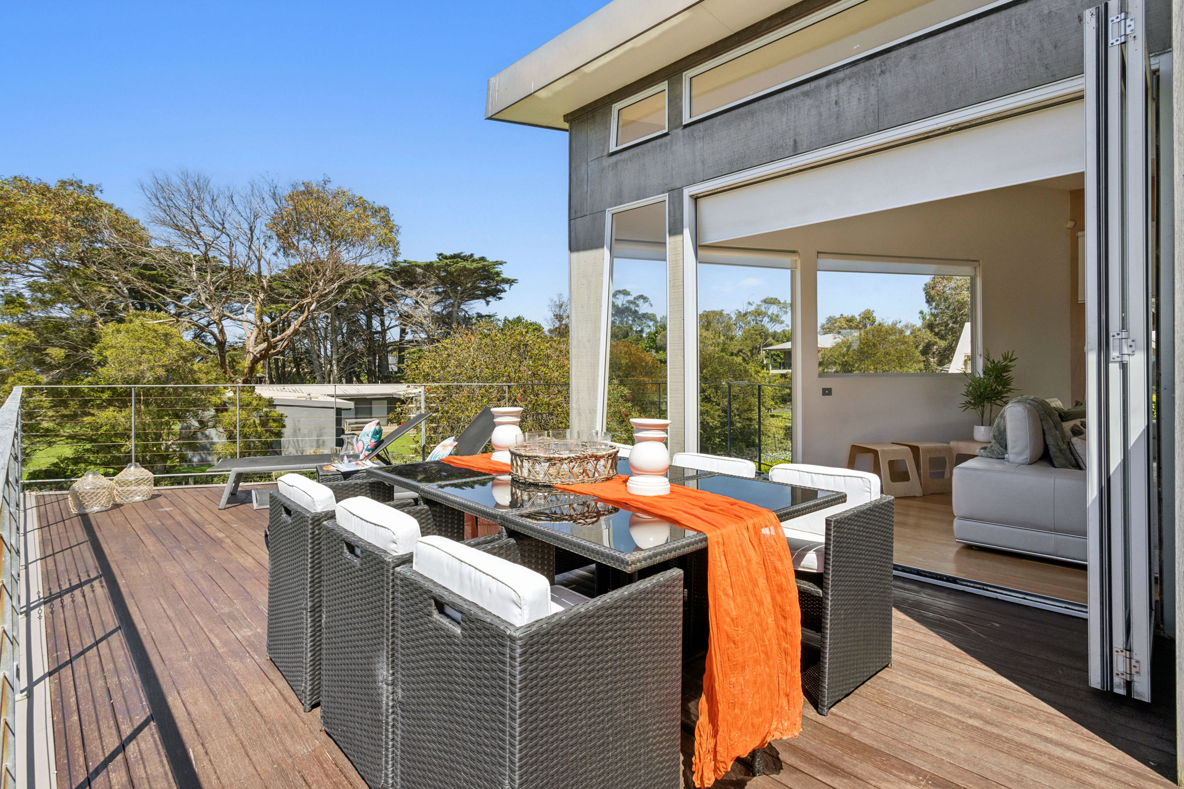 A modern outdoor deck with wicker furniture and a glass table, overlooking a residential area.
