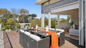Una terraza moderna al aire libre con mobiliario de mimbre y una mesa de vidrio, con vistas a una zona residencial.