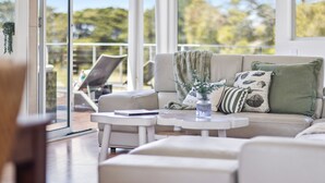 A modern living room with a sofa, two side tables, and a coffee table. There is a balcony with a chair and a plant. - Fairway View (FLINDERS)