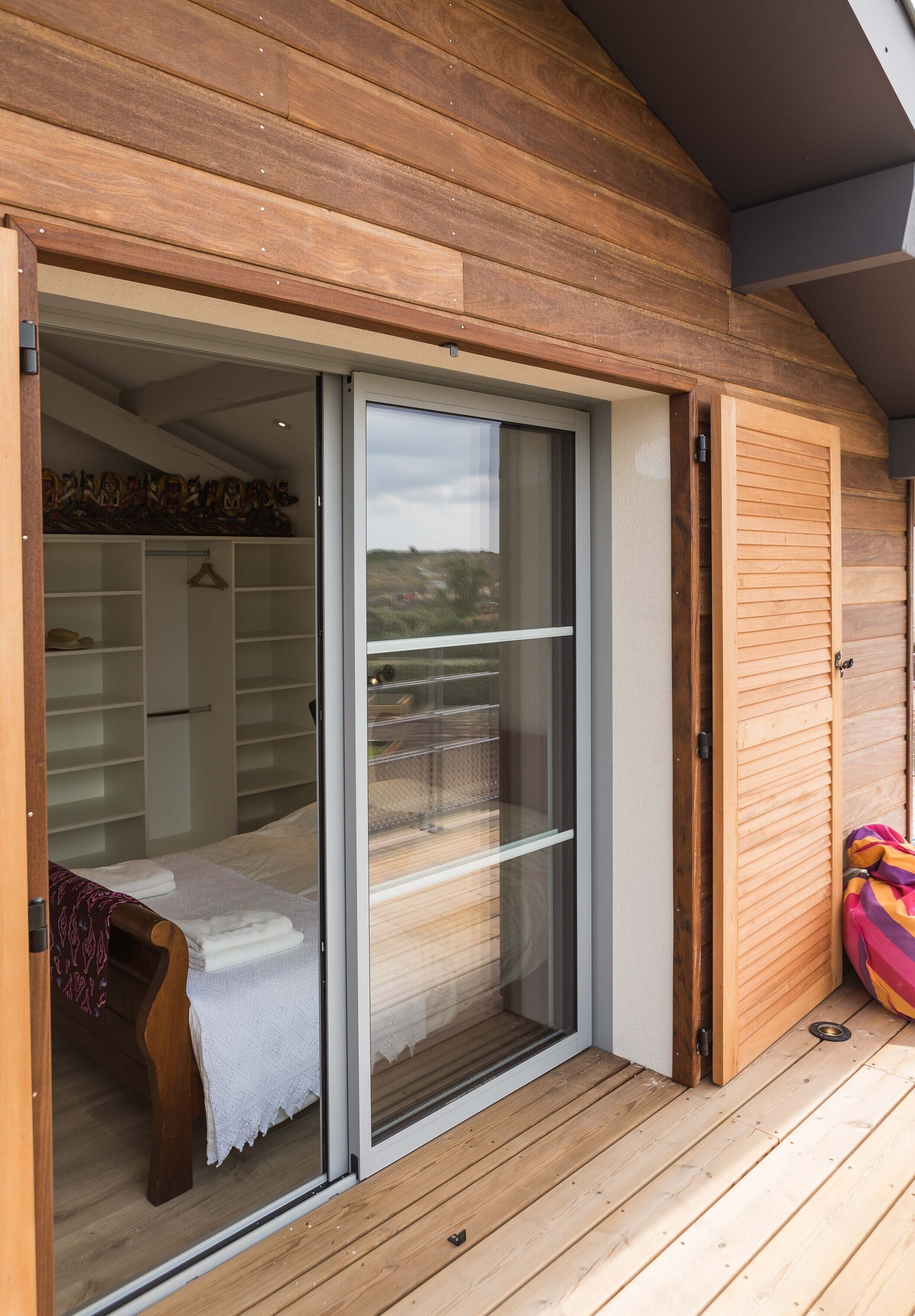 Ein Holzfassade mit einer Schiebetür, die zu einem Schlafzimmer mit einem Bett und einer weißen Bank führt.
