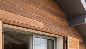 Exterior de madera con puerta corrediza de vidrio que da a un dormitorio con cama y un banco blanco.