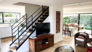 Una sala moderna con una escalera, un televisor de pantalla plana, un comedor con asientos exteriores y un ventanal grande.