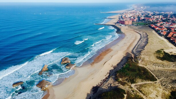 Vista aérea de un pueblo costero con playa, afloramientos rocosos y edificios residenciales.
