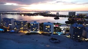 A coastal cityscape at dusk with high-rise buildings, a marina, and a beach area with pools. - 2 Steps to the Beach 2 bedroom apartment (Zona Hotelera)
