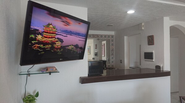 A modern interior with a flat-screen TV mounted on the wall, a reception desk, and a small shelf with books.