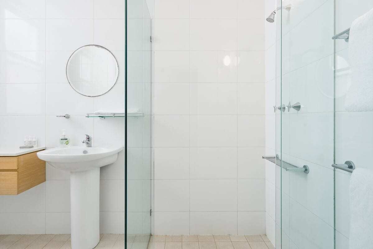 Une salle de bain moderne avec une douche à parois de verre, un lavabo sur colonne et un miroir rond.