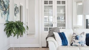 Een witte kamer met een witte bank, een glazen kast en een grote spiegel.