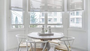 Een hoekzaal met een ronde tafel en stoelen, grote ramen en uitzicht op gebouwen.