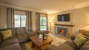 Una sala de estar con chimenea, un conjunto de sofás, una mesa de centro con botellas y un televisor montado en la pared.