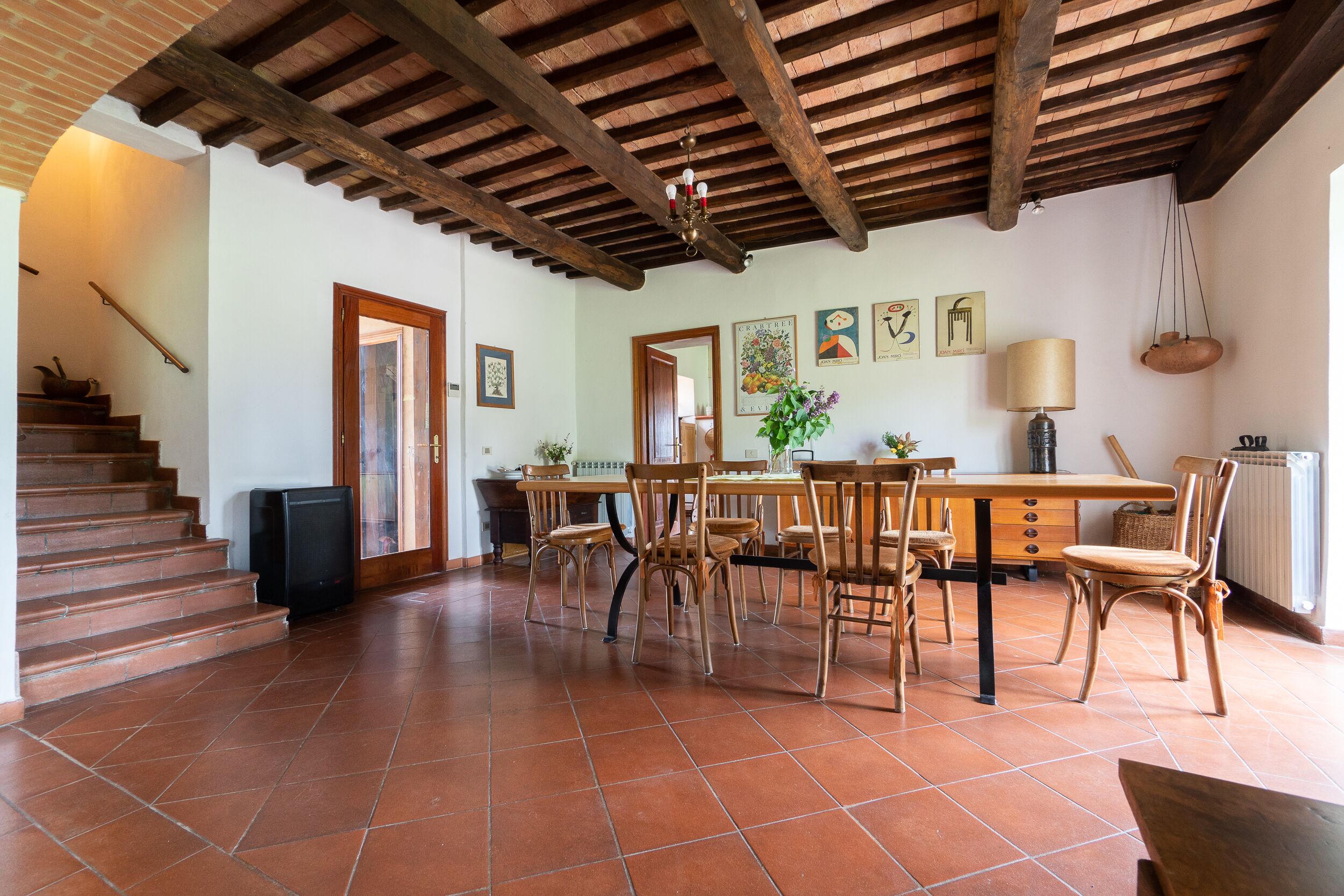 A spacious dining area with a wooden table and chairs, a staircase leading to an upper level, and a rustic ceiling with exposed beams.