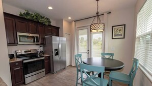 A modern kitchen with dark wood cabinets, stainless steel appliances, and a teal dining table with chairs. - Gator Cove: Quaint 2-bedroom, 1-bath cottage, sleeps 4. Great for a peaceful retreat. (Oviedo)