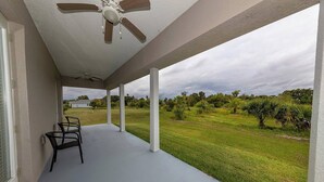 A covered porch with a ceiling fan, a concrete floor, and a view of a grassy field with trees. - Gator Cove: Quaint 2-bedroom, 1-bath cottage, sleeps 4. Great for a peaceful retreat. (Oviedo)