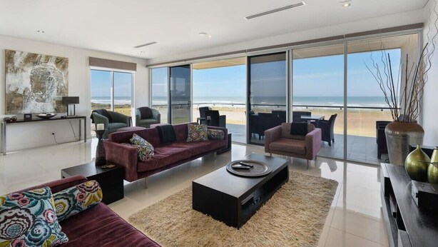 A modern living room with a large window, a sofa, a coffee table, and a view of the beach. - 52 Esplanade - Luxury - Seafront - Wi-Fi (Middleton)