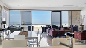 A spacious room with a large window offering a view of the beach, a dining area with a table and chairs, and a seating area with sofas and a coffee table. - 52 Esplanade - Luxury - Seafront - Wi-Fi (Middleton)