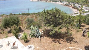 Paesaggio costiero con una spiaggia, auto parcheggiate e una strada.