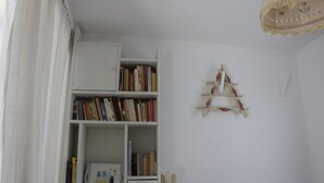 Una stanza con una libreria bianca piena di libri, un piccolo mobiletto bianco e una scala di legno decorativa sulla parete.