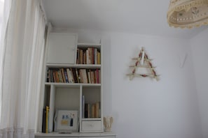 A room with a white bookshelf filled with books, a small white cabinet, and a decorative wooden ladder on the wall. - Aegean traditional home in Athens Riviera (Thimari)