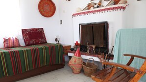 Una stanza con un letto, una sedia di legno, un caminetto e una parete decorata con conchiglie e un cuscino rosso con motivo.