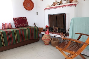 A room with a bed, a wooden chair, a fireplace, and a wall decorated with shells and a red patterned pillow. - Aegean traditional home in Athens Riviera (Thimari)