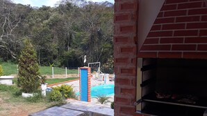 A patio area with a barbecue grill, a swimming pool, and a view of a mountainous landscape. - Mini Chácara Campo Verde Ibiúna SP<br>A cozy and simple place to relax (Ibiúna)