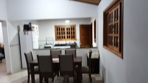 A dining area with a table and chairs, a kitchen in the background, and a window with a wooden frame. - Mini Chácara Campo Verde Ibiúna SP<br>A cozy and simple place to relax (Ibiúna)
