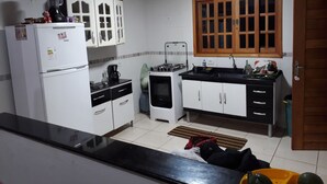 A compact kitchen with white cabinets, a black countertop, a refrigerator, a stove, and a window with wooden frames. - Mini Chácara Campo Verde Ibiúna SP<br>A cozy and simple place to relax (Ibiúna)