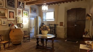 Una habitación tradicional con una mesa de madera, un jarrón grande con flores secas y una puerta de madera rústica.