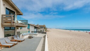 Une propriété située en bord de mer, dotée d’une terrasse en bois, de chaises longues et d’un espace piscine.