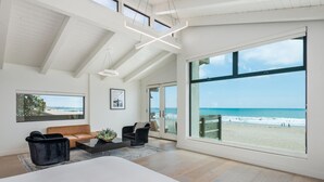 Une chambre spacieuse avec un grand lit, un canapé et une table basse. Elle dispose de grandes fenêtres offrant une vue sur la plage et d’un design moderne au niveau du plafond.